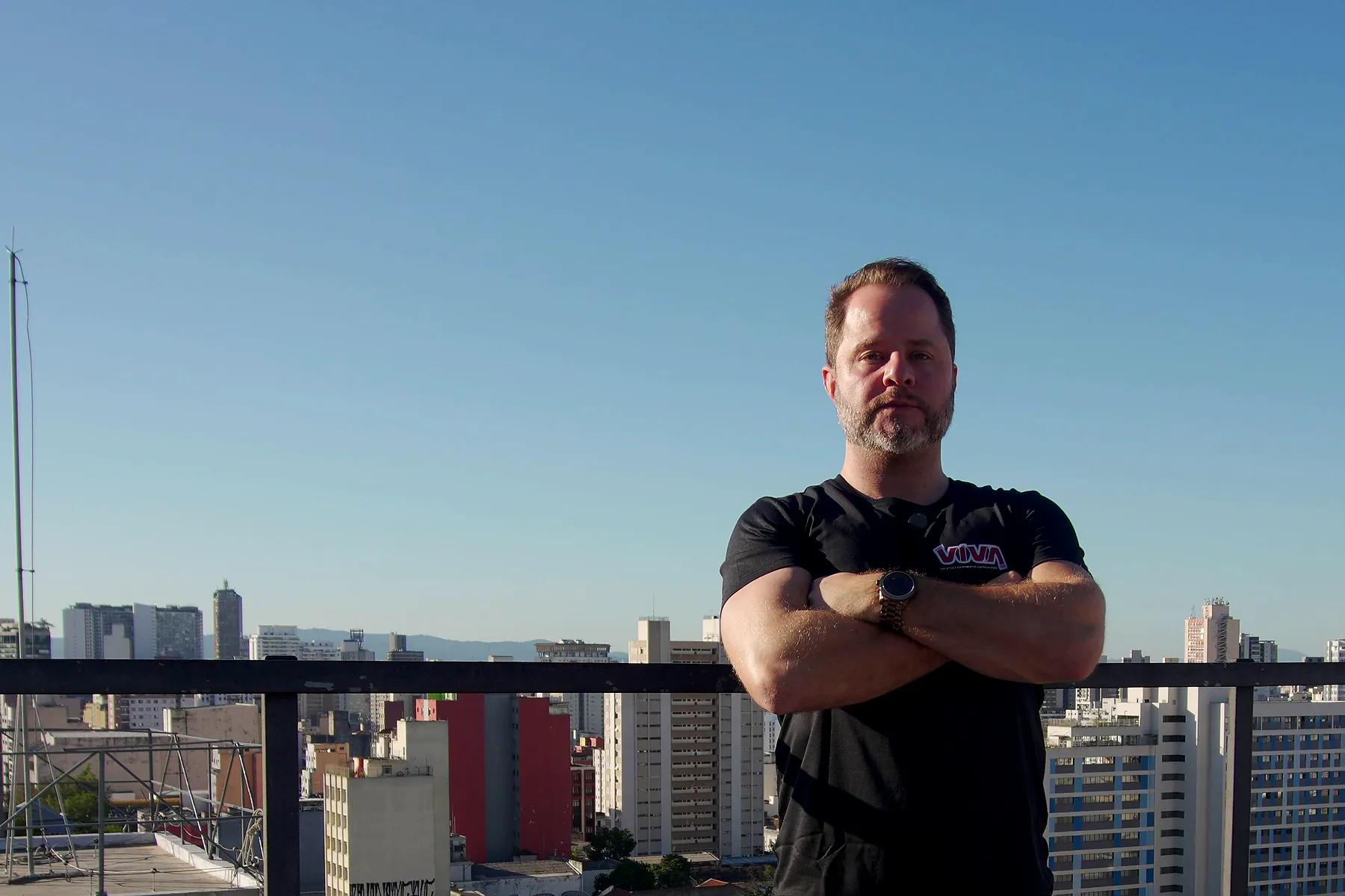 Felipe, da VIVA, de braços cruzados numa cobertura, com a cidade de São Paulo ao fundo